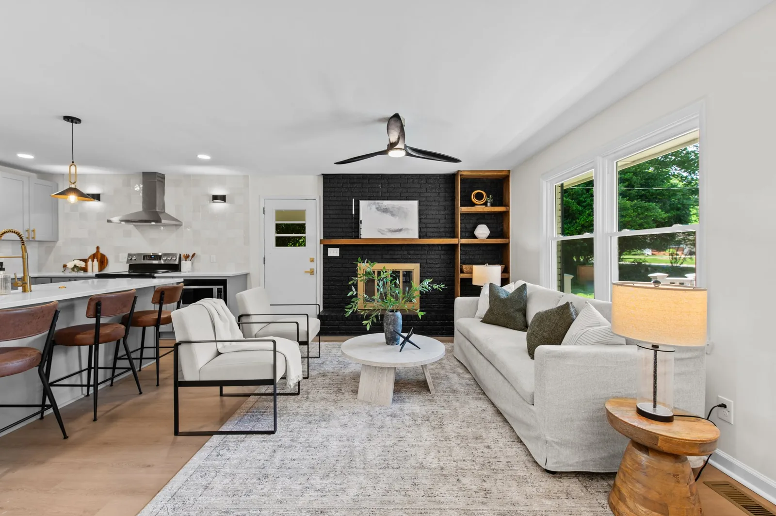 Roxanne open living room and kitchen with a black brick fireplace, wood floors, and island seating
